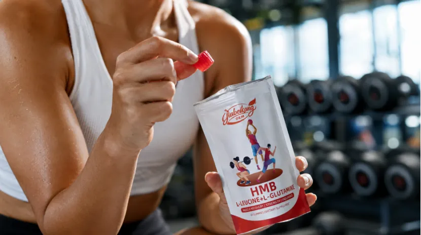 Woman in a gym holding an HMB gummy and pouch